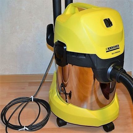 The appearance of the model Karcher WD 3 Premium The vacuum cleaner is stored in the corner of the room.